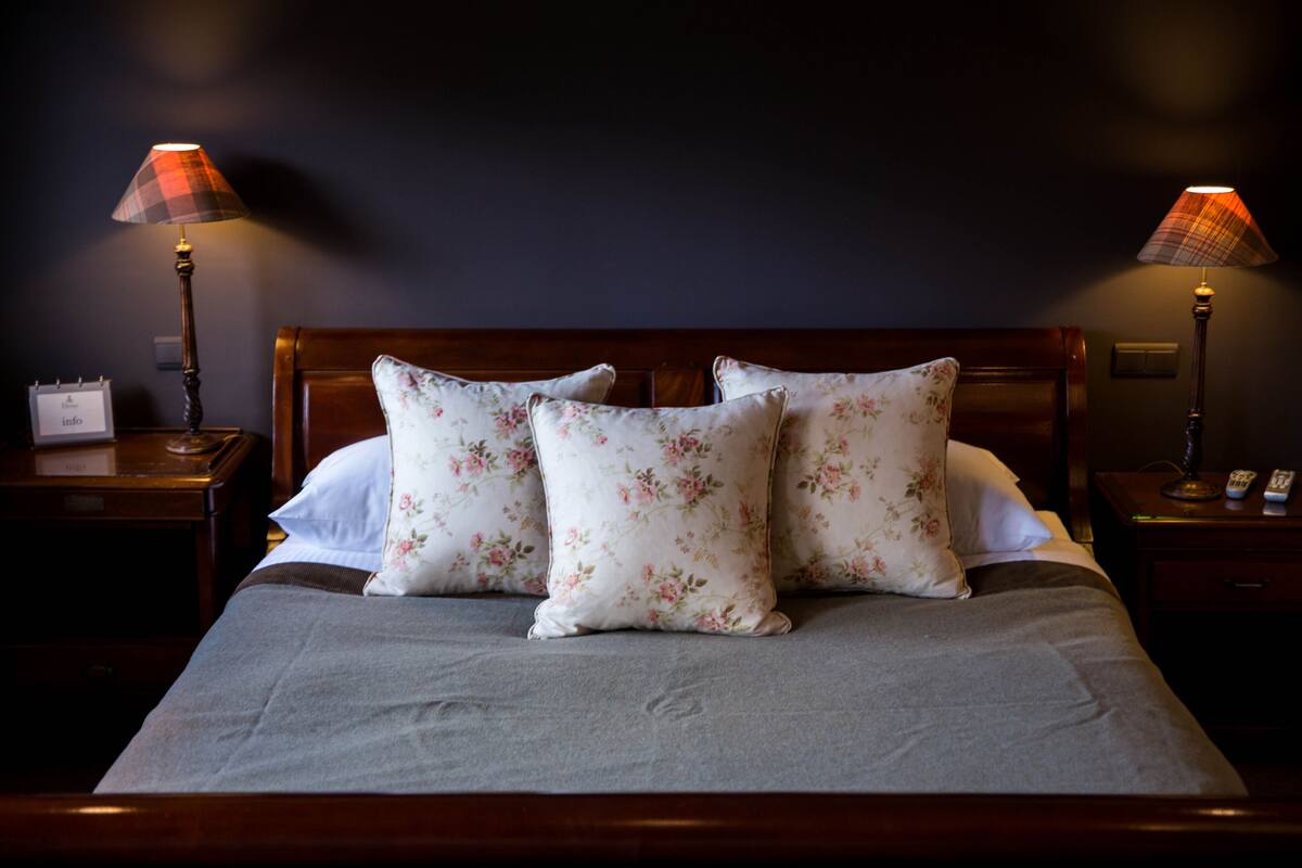 A neatly made bed with floral pillows, a grey bedspread, and two bedside lamps on wooden nightstands.