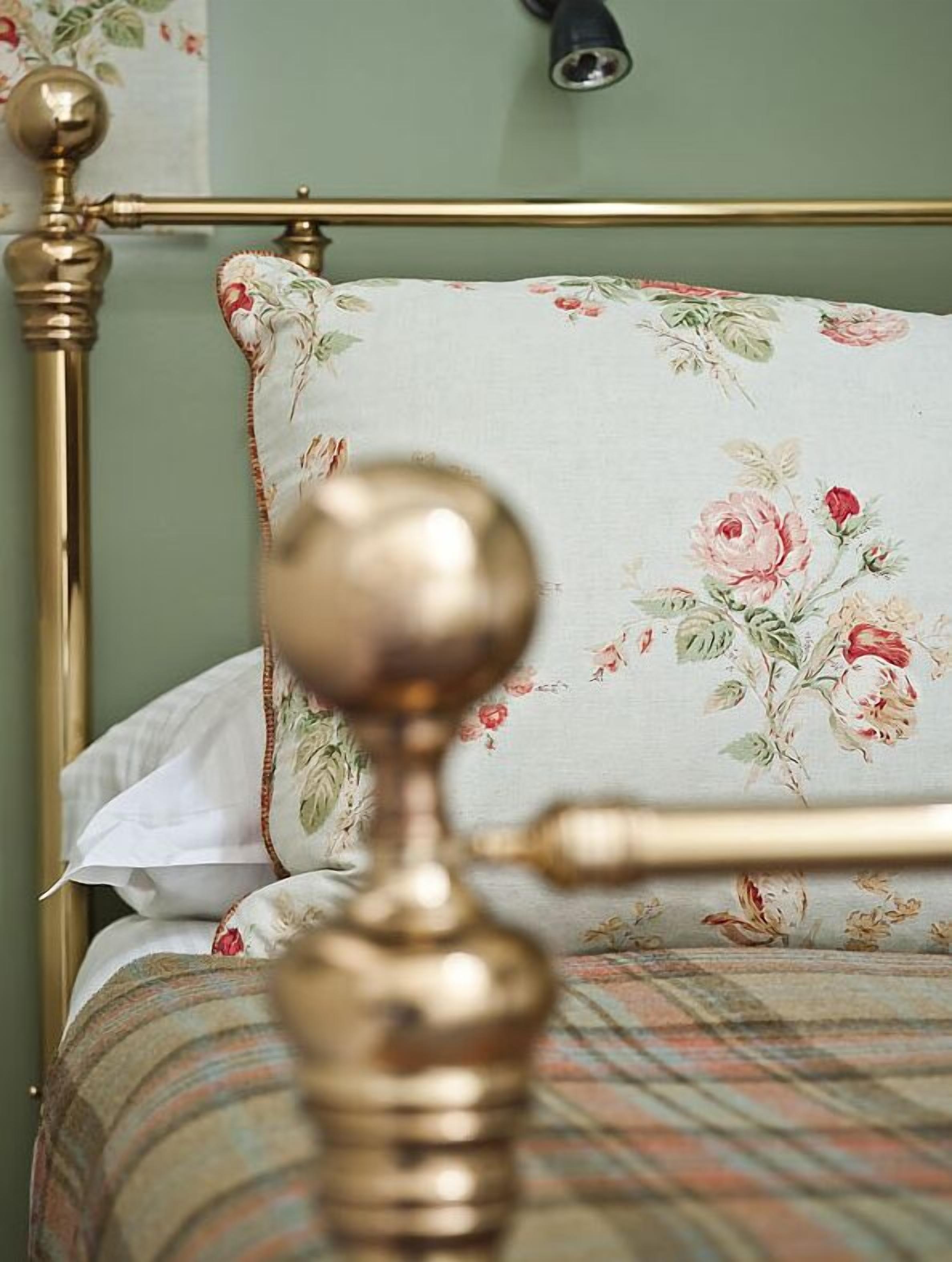 A bed with a floral-patterned pillow and a brass headboard.