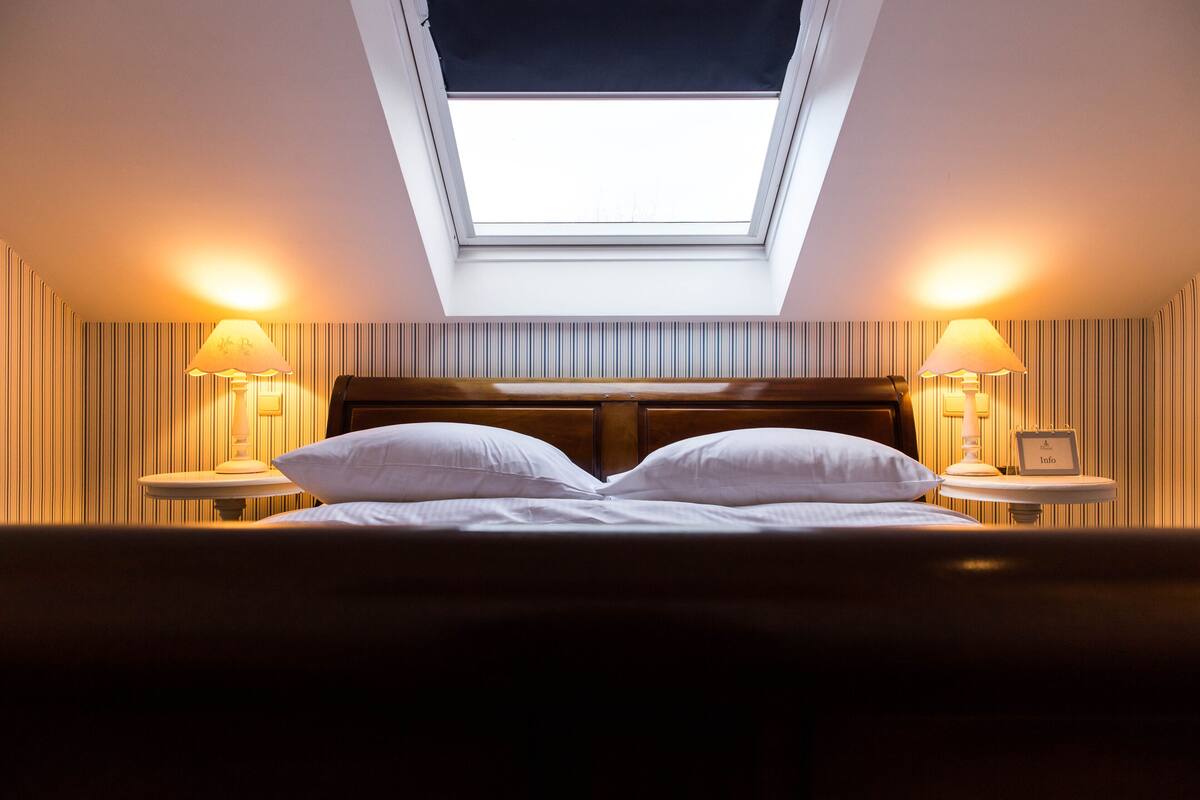 A hotel room with a skylight, a bed with white linens, two bedside lamps, and striped wallpaper.