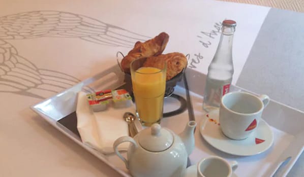 A breakfast tray with croissants, juice, a bottle, and a teapot on a table. - Au Cadran Bleu (Levallois-Perret)