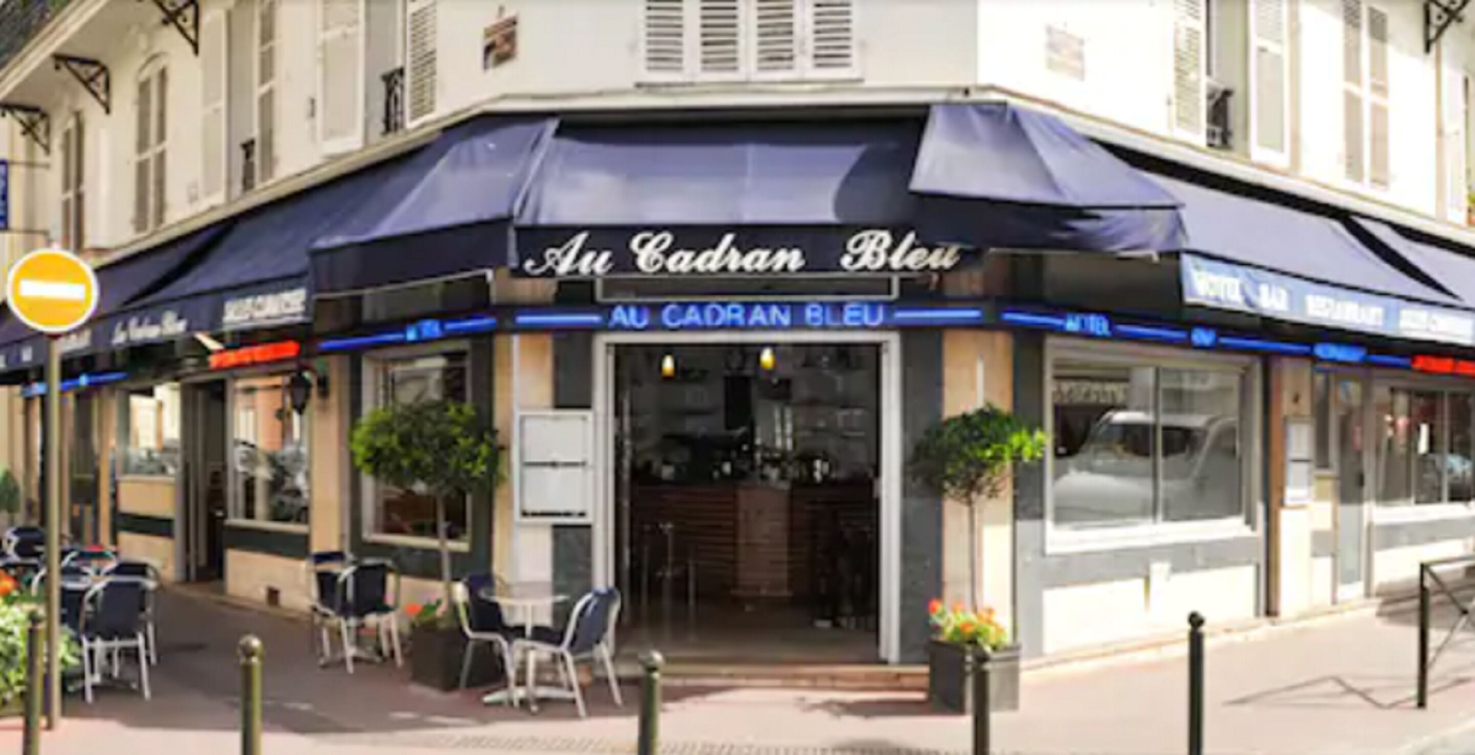 Un restaurante llamado 'Au Cadran Bleu' con terraza y un letrero que indica restaurante y hotel.