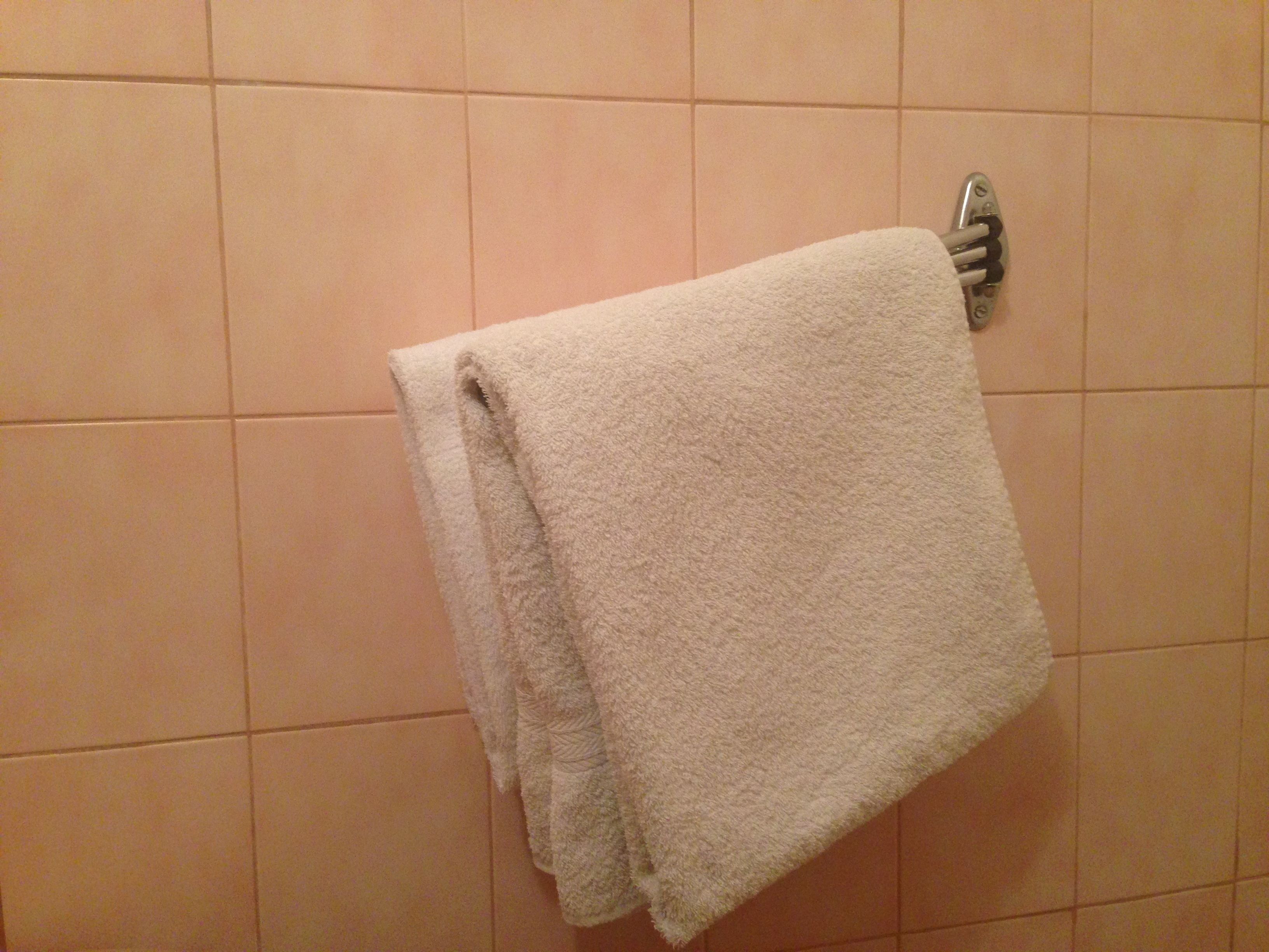 Een witte handdoek hangt aan een metalen handdoekhouder voor een betegelde muur.