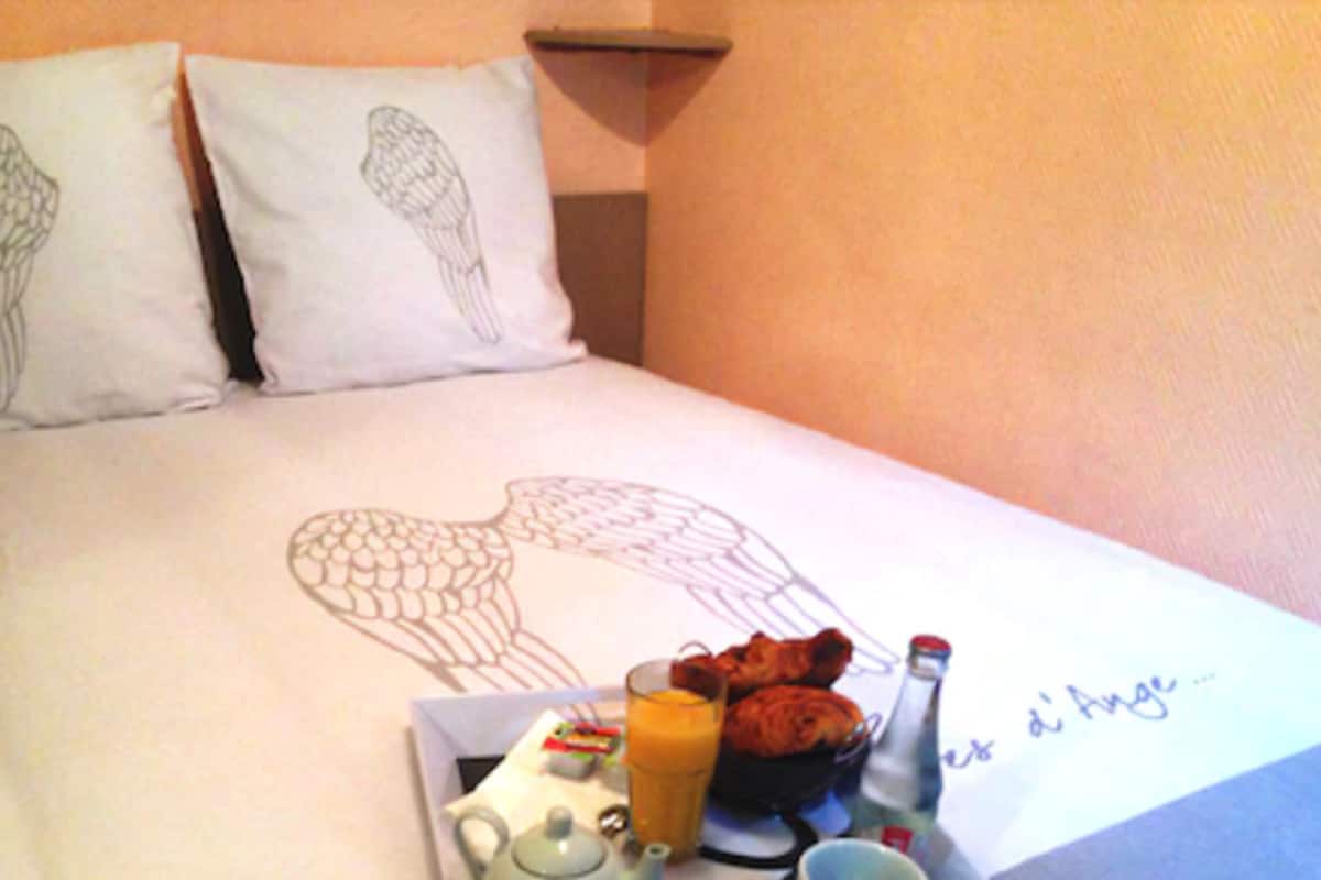 A bed with a heart-shaped design, pillows with wing patterns, and a breakfast tray with eggs, juice, and a bottle.