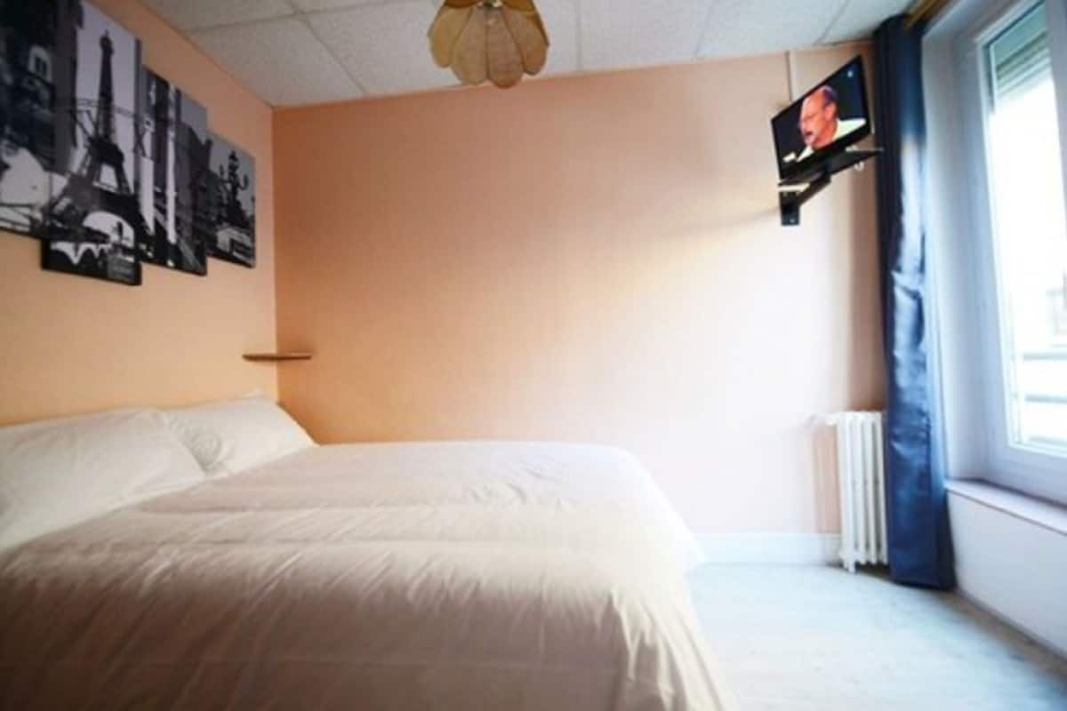 A bedroom with a bed, a wall-mounted TV, and a window with curtains.