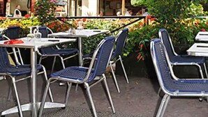 Espace extérieur aménagé avec des chaises et des tables en métal, entouré de plantes et de fleurs en pot.
