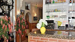 Un espace bar avec un comptoir en briques, un vase jaune orné de fleurs et des étagères remplies de bouteilles et de verres.