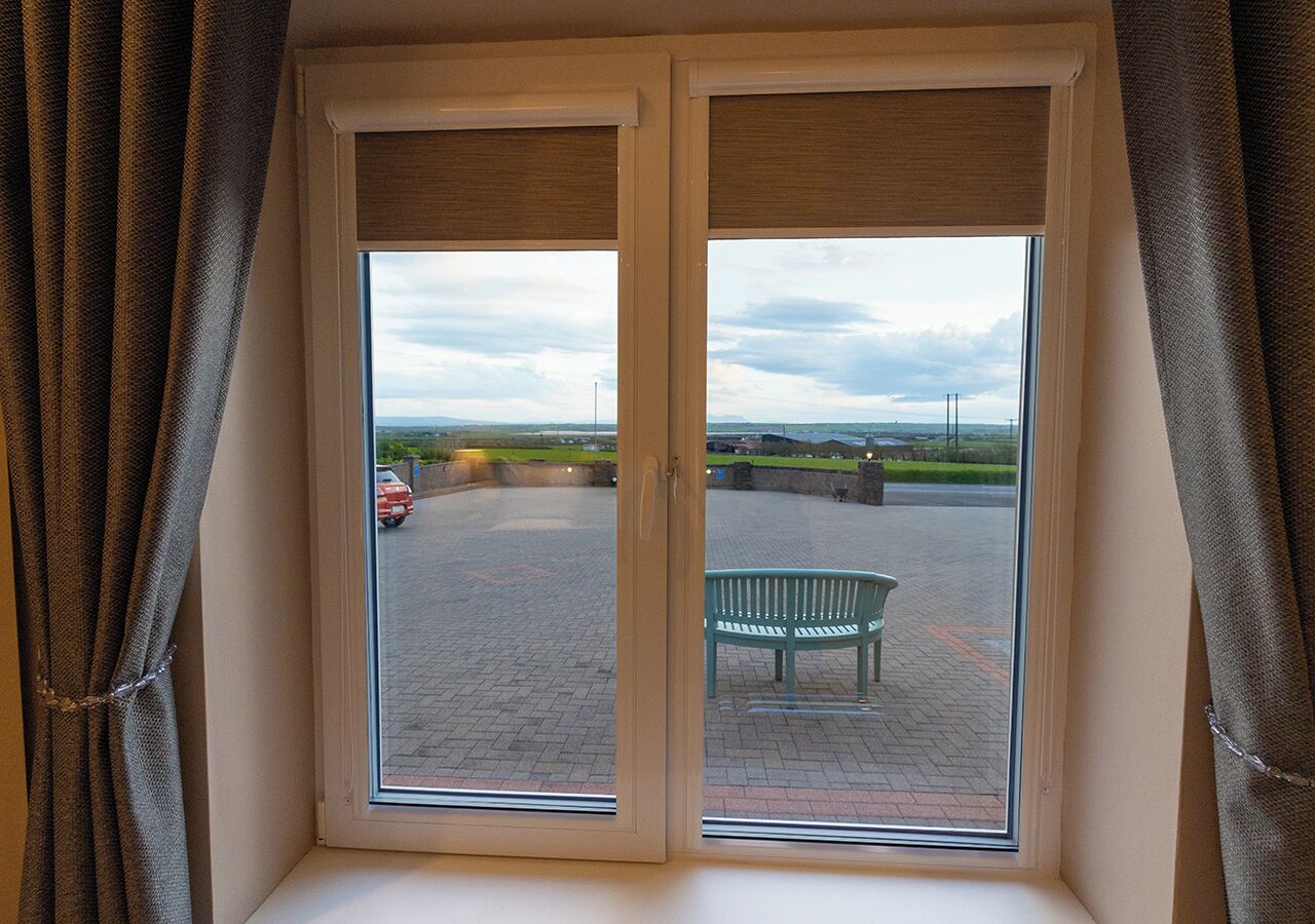Una ventana con vistas a un espacio exterior que incluye una zona pavimentada y un banco.