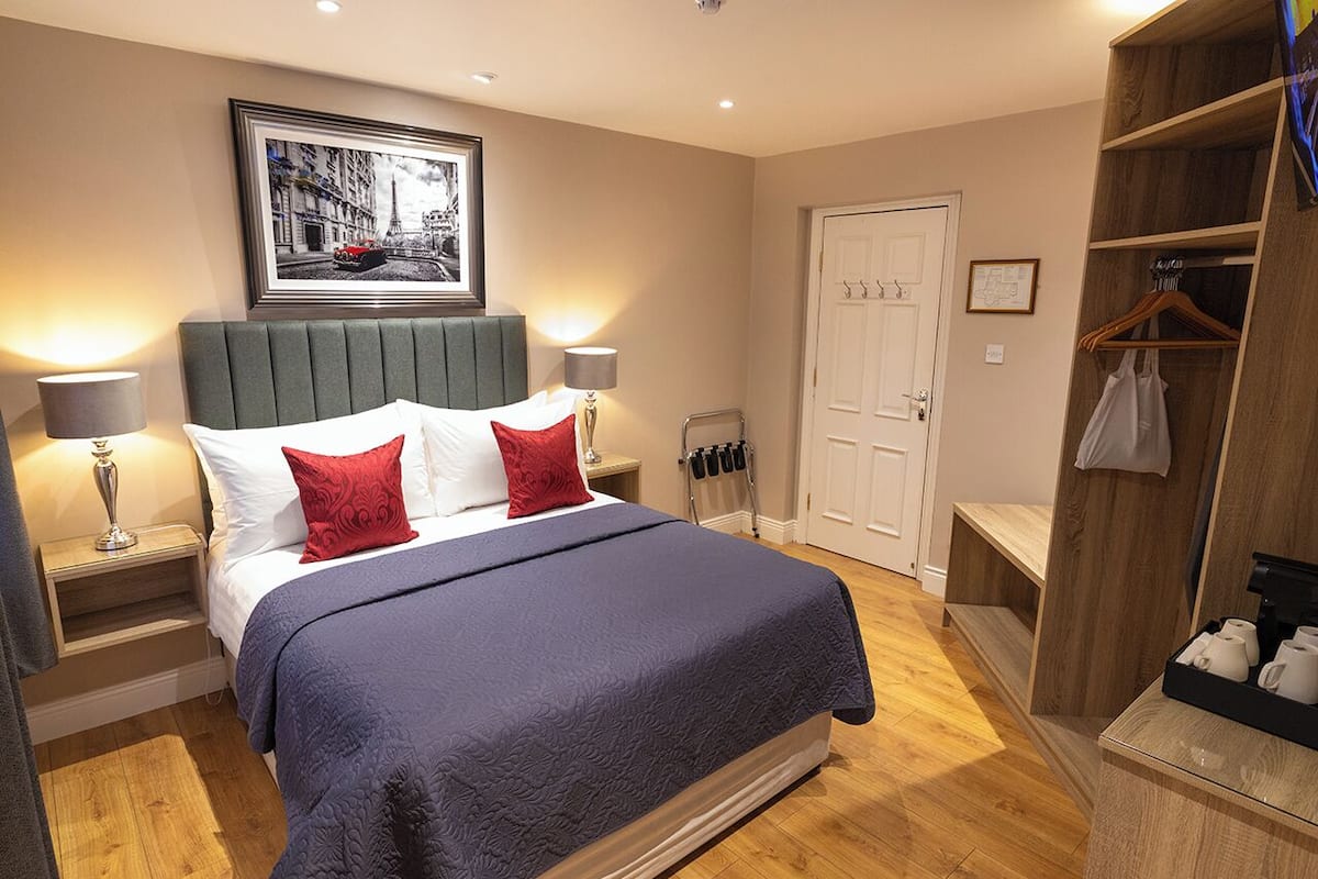 A bedroom with a bed, bedside lamps, a wardrobe, a door, and a framed picture on the wall.
