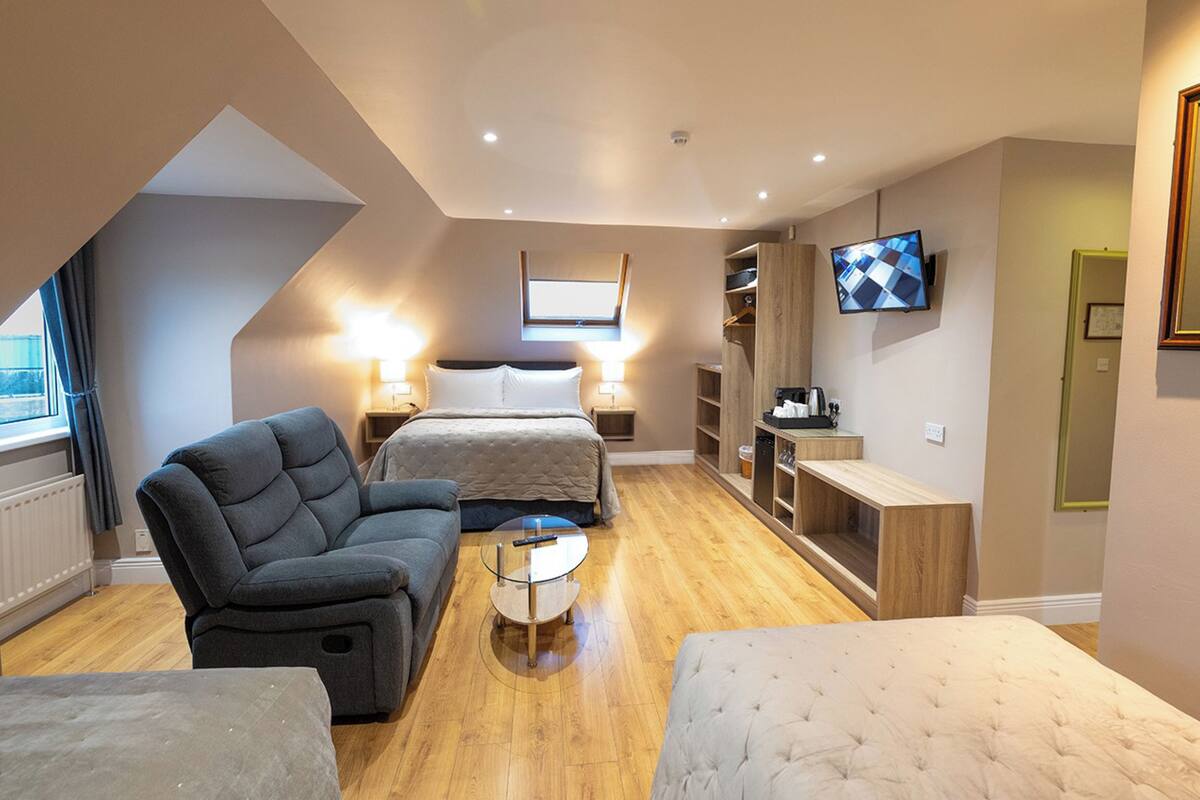 A modern hotel room with a loft bed, a sofa, a coffee table, and a TV mounted on the wall.