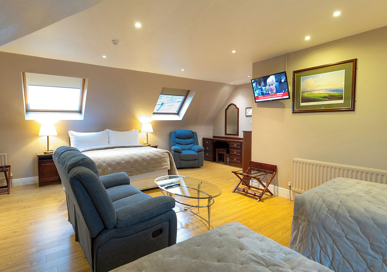 Een slaapkamer met een bed, twee stoelen, een kleine tafel, een televisie en een ingelijste foto aan de muur.