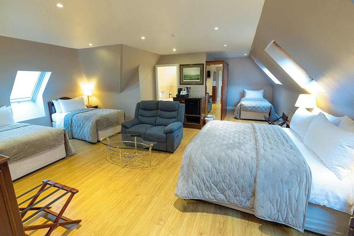 A spacious room with two beds, a sofa, a chair, a small table, and a TV.