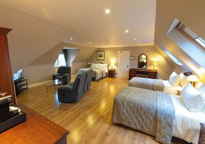 A spacious room with a sloped ceiling, two beds, a seating area with a sofa and chairs, a television, and a wooden floor. - The Tides B&B (Ballybunion)