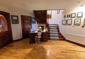 A spacious room with a wooden floor, a desk with a chair, a staircase, and framed awards on the wall. - The Tides B&B (Ballybunion)