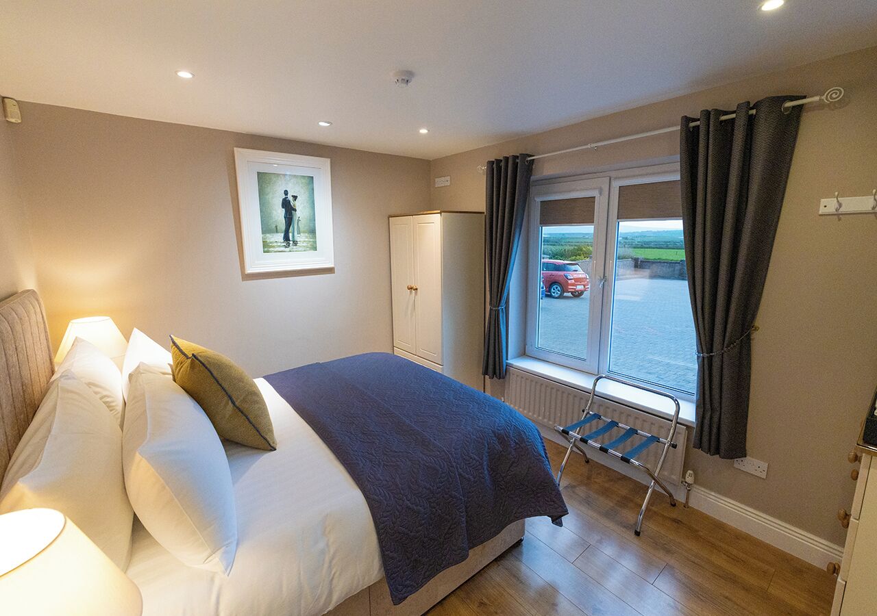 A bedroom with a bed, a radiator, a window with curtains, a wardrobe, and a picture on the wall.