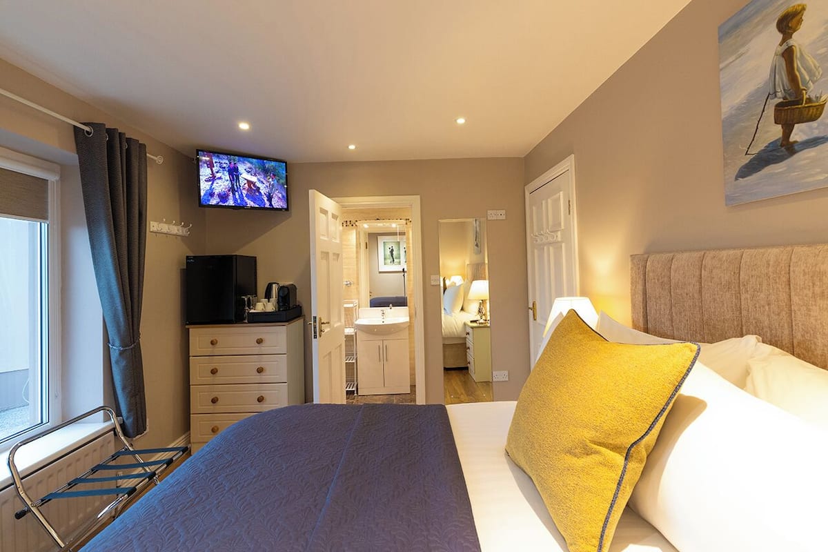 A hotel room with a bed, a television, a bathroom, and a painting on the wall.