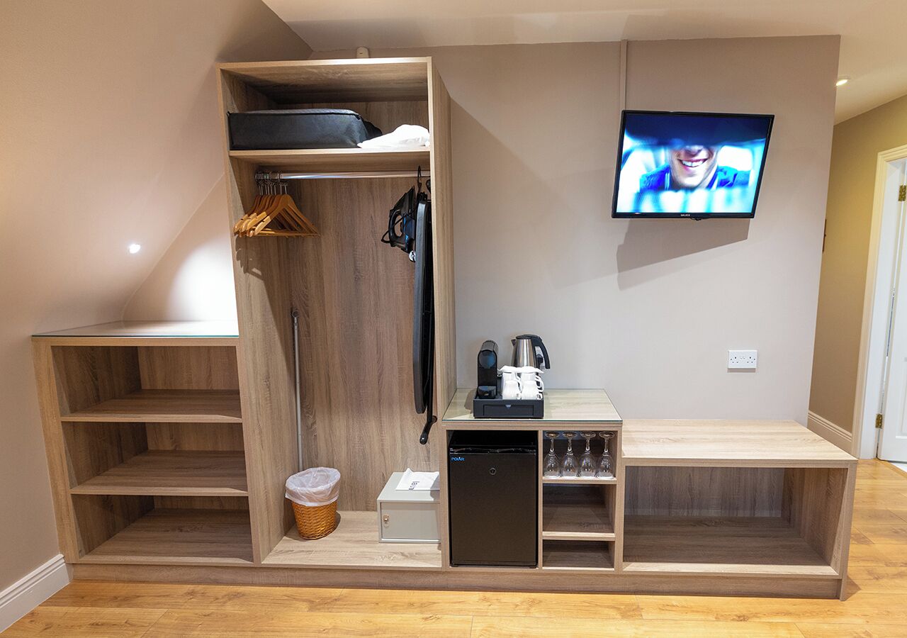 A compact room with a built-in wardrobe, a small kitchenette, a television, and a glass partition.