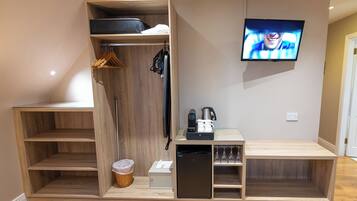 A compact room with a built-in wardrobe, a small kitchenette, a television, and a glass partition.