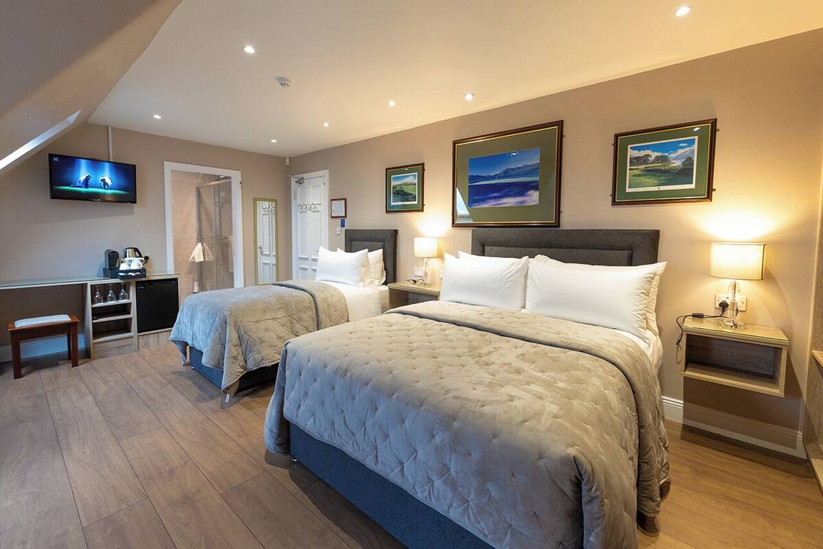 A hotel room with two beds, a desk, a TV, and artwork on the walls.