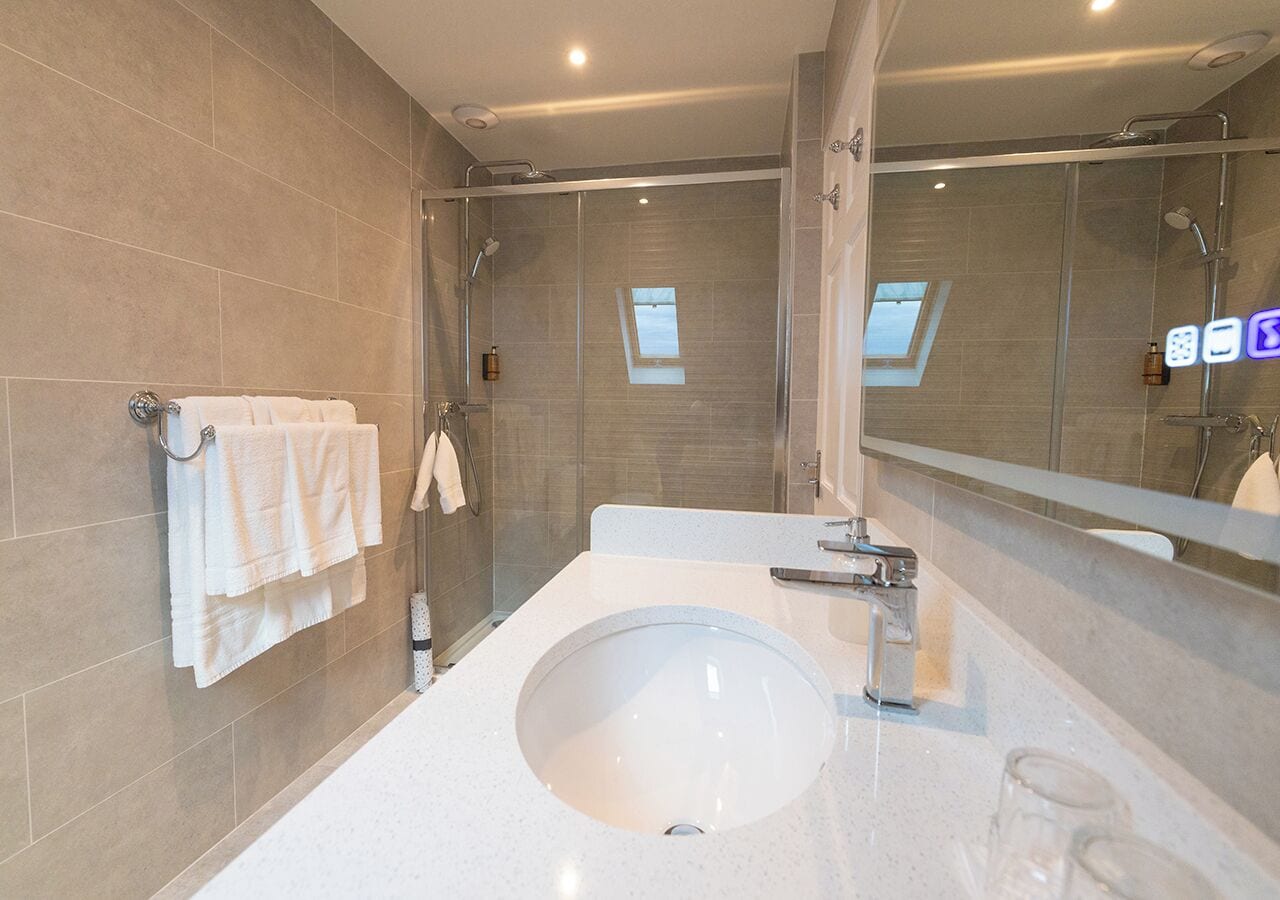 Un bagno moderno con un lavandino ampio, un box doccia in vetro e un portasciugamani con asciugamani bianchi.