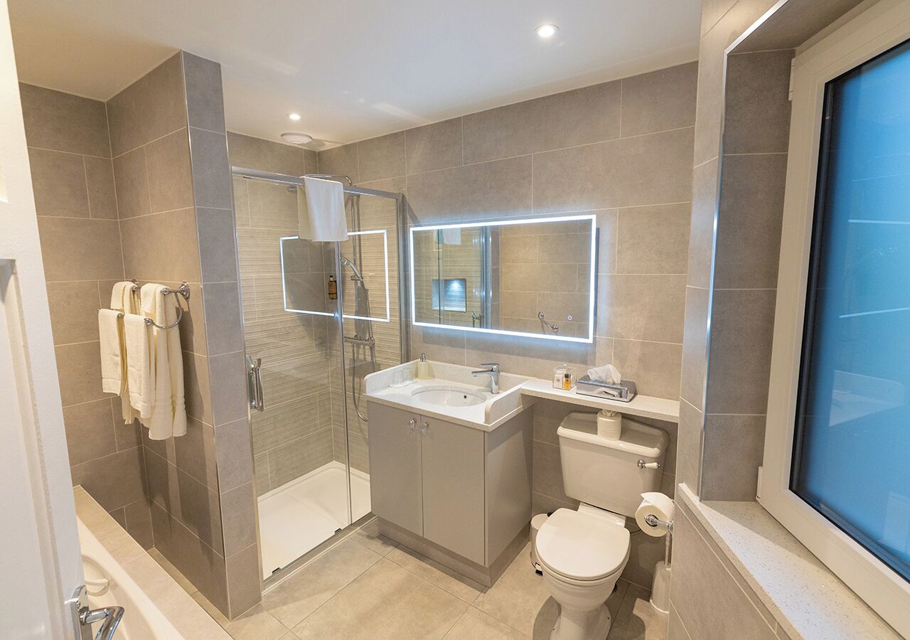 Un baño moderno con ducha envuelta en vidrio, tocador con espejo y inodoro.