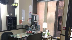 Una oficina con un mostrador de recepción, un reloj, una computadora, una lámpara y un ventanal con vistas al exterior.