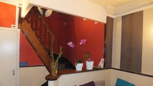 Una escalera con barandilla de madera que conduce a una pared roja. Hay plantas en macetas sobre la pared y un sofá con cojines.