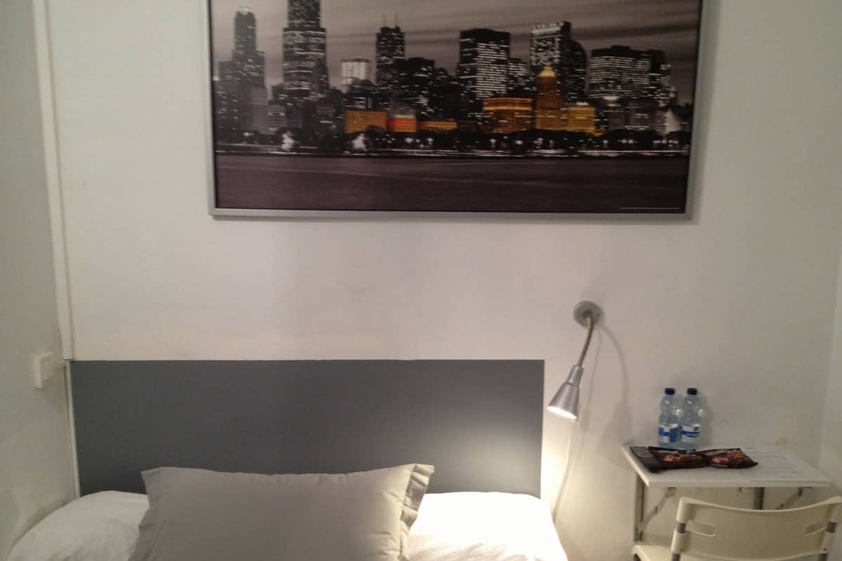 Habitación de hotel con cama, mesita de noche con lámpara, una silla y vista panorámica de la ciudad.