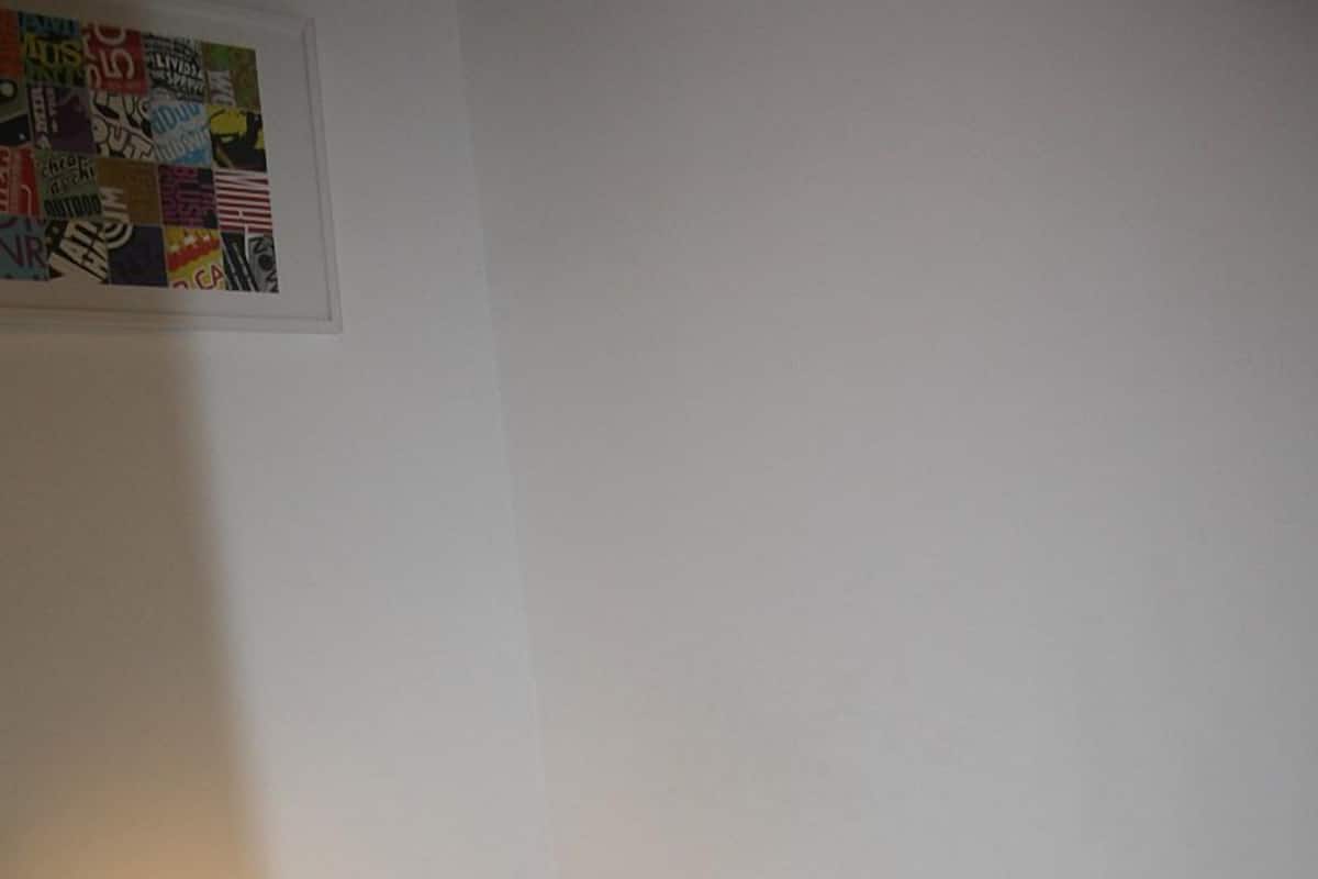 Una habitación pequeña y ordenada con una cama individual, una mesita de noche, una lámpara y una luz en la pared.