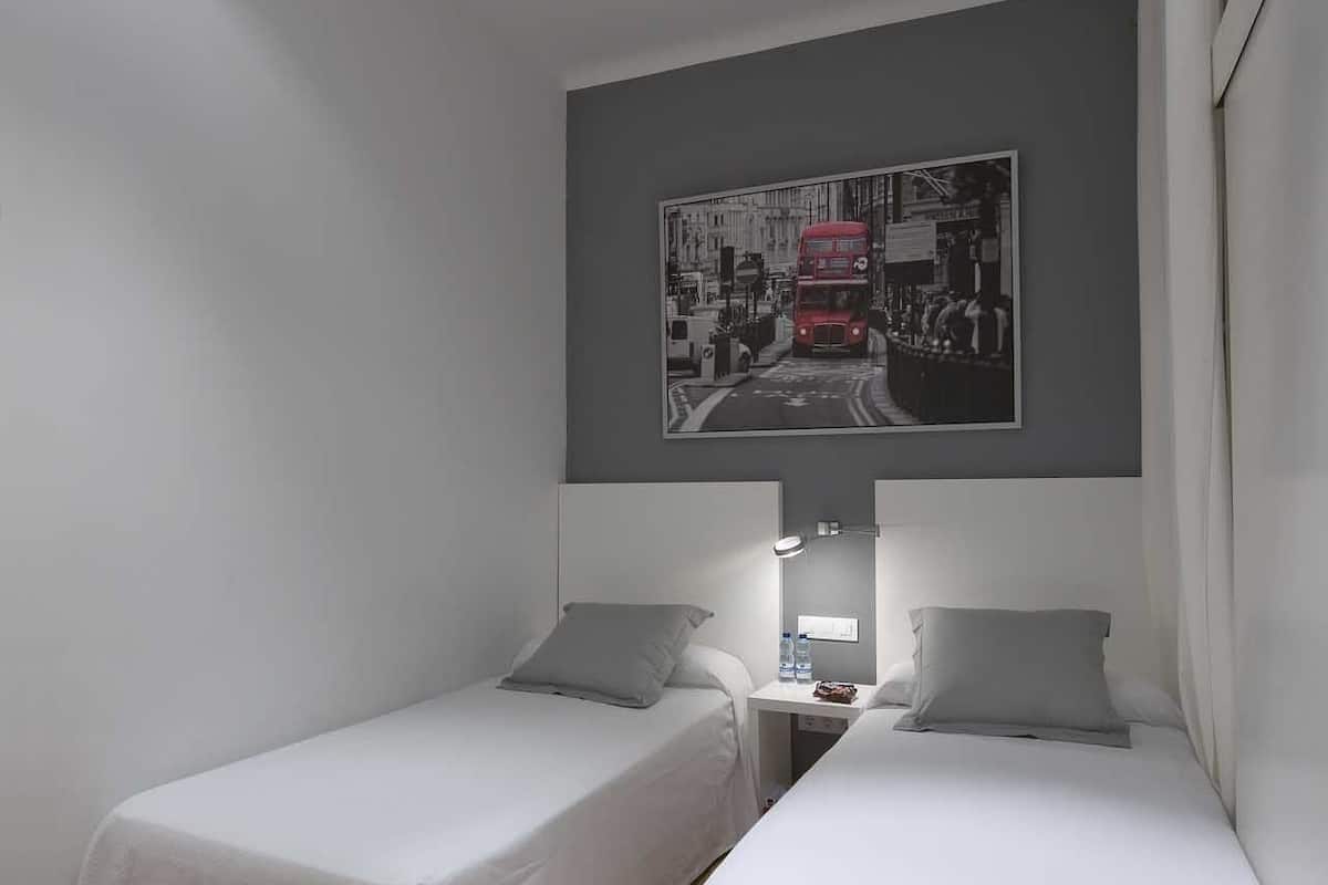 Una habitación con dos camas individuales, una mesita de noche con lámpara y un cuadro en la pared.