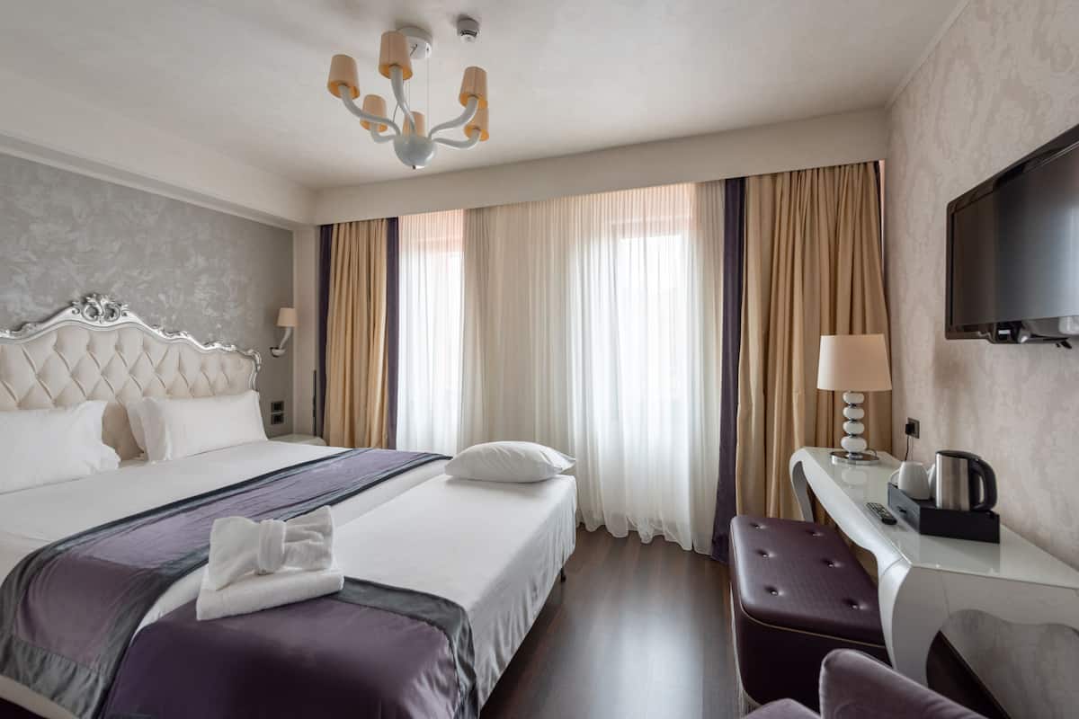 A hotel room with a large bed, a desk with a lamp, a television, and a window with curtains.