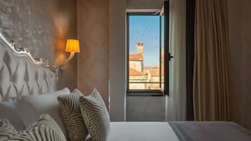 Habitación de hotel con cama, almohadas, una lámpara de pared y una ventana que ofrece vistas a edificios y aves.