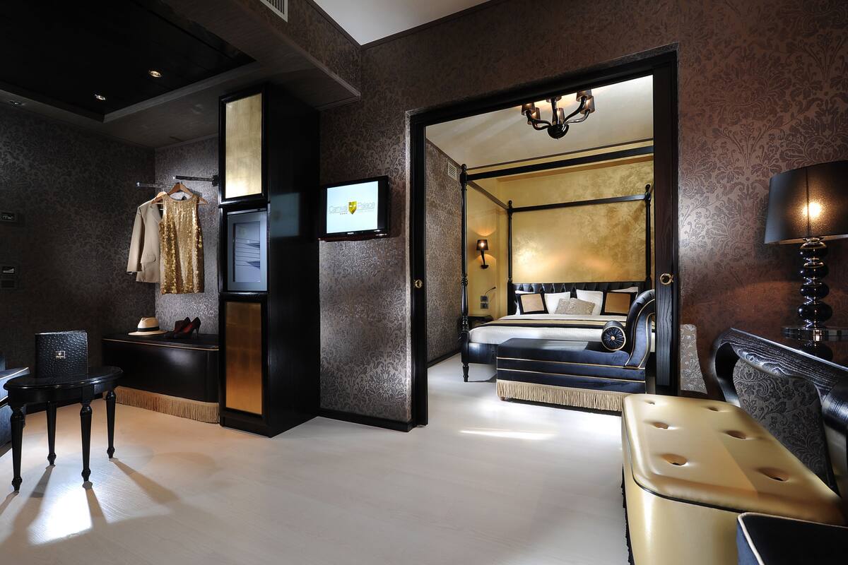 A modern hotel room with a large bed, a sitting area with a sofa and armchair, a small table, and a television.
