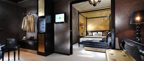 A modern hotel room with a large bed, a sitting area with a sofa and armchair, a small table, and a television.