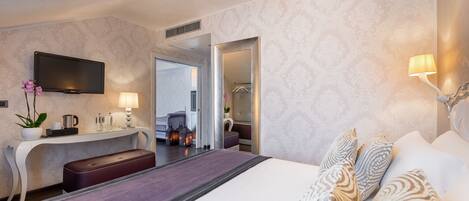 Una habitación de hotel moderna con una cama grande, un escritorio con televisión de pantalla plana, un espejo y un baño visible a través de una puerta abierta.