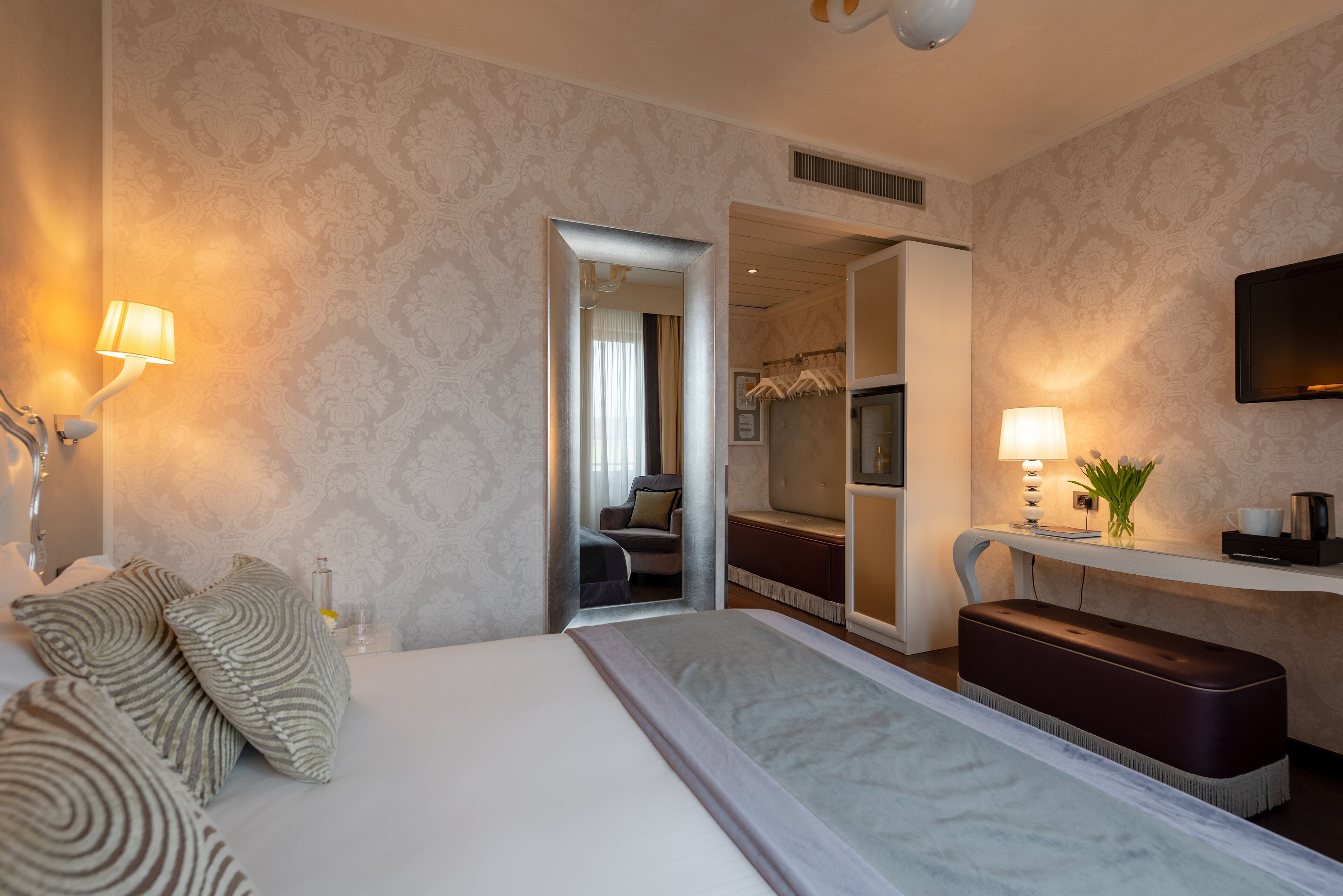 A hotel room with a large bed, bedside lamps, a mirror, a seating area, and a television.