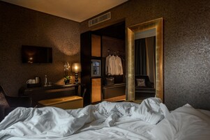Hotellihuone, jossa on sänky, kirjoituspöytä lampun kanssa, televisio ja vaatekaappi.