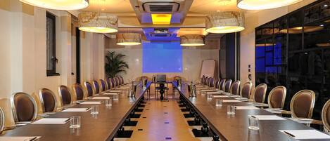 Un salón de conferencias con una larga mesa, sillas e iluminación colgante.