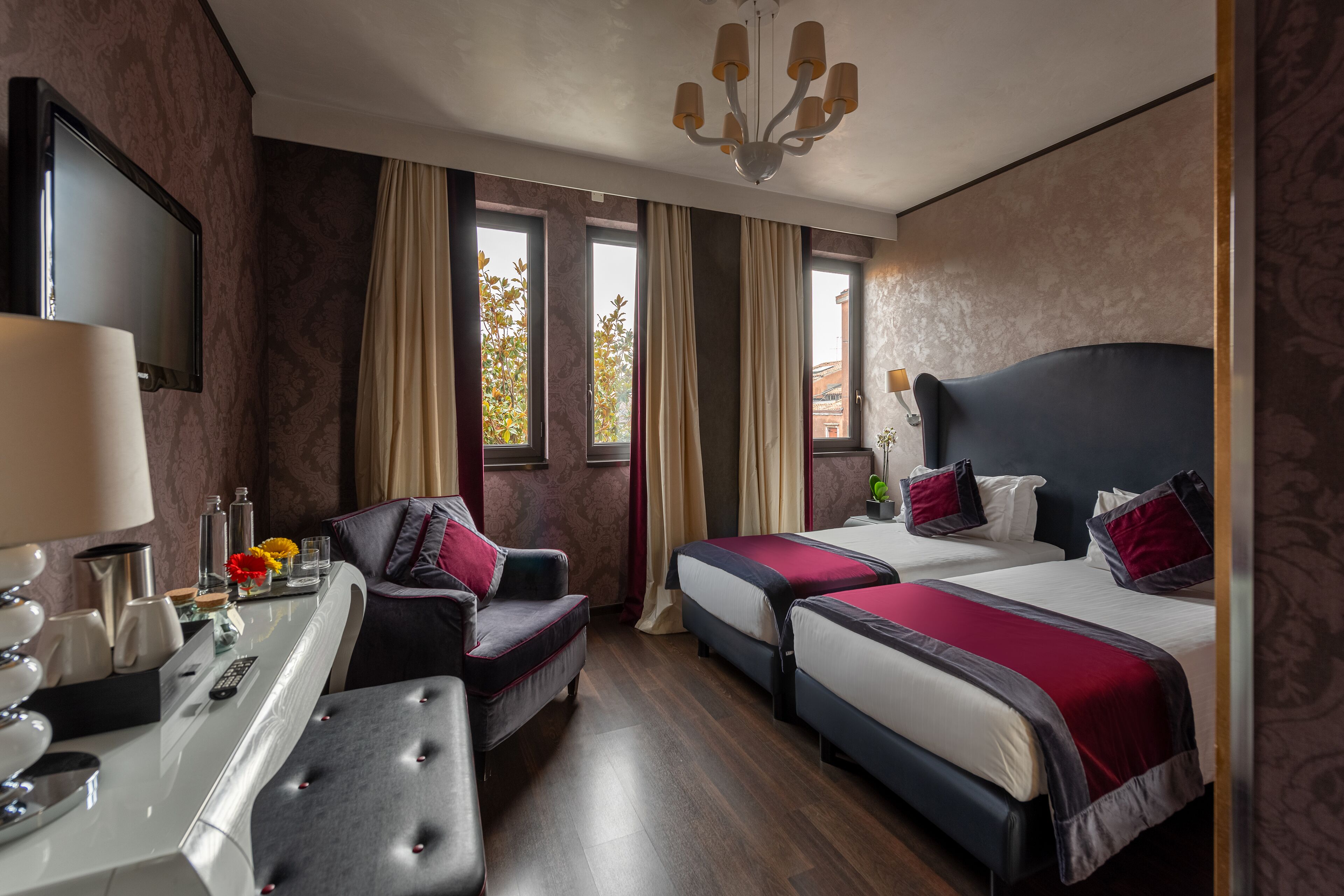 A hotel room with two beds, a desk, a chair, and a TV.