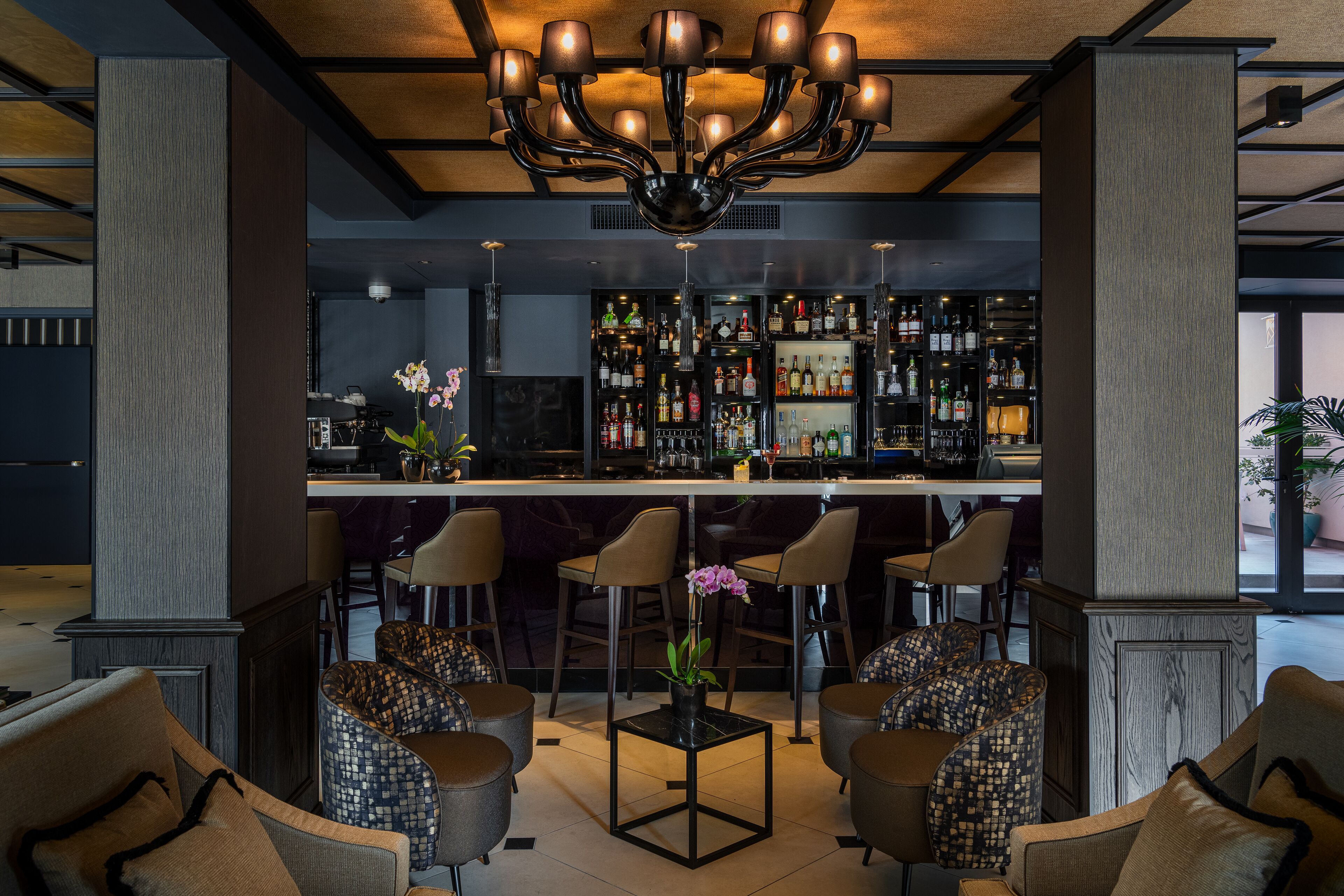 A bar area with a central bar, multiple seating options, and a variety of bottles on shelves.
