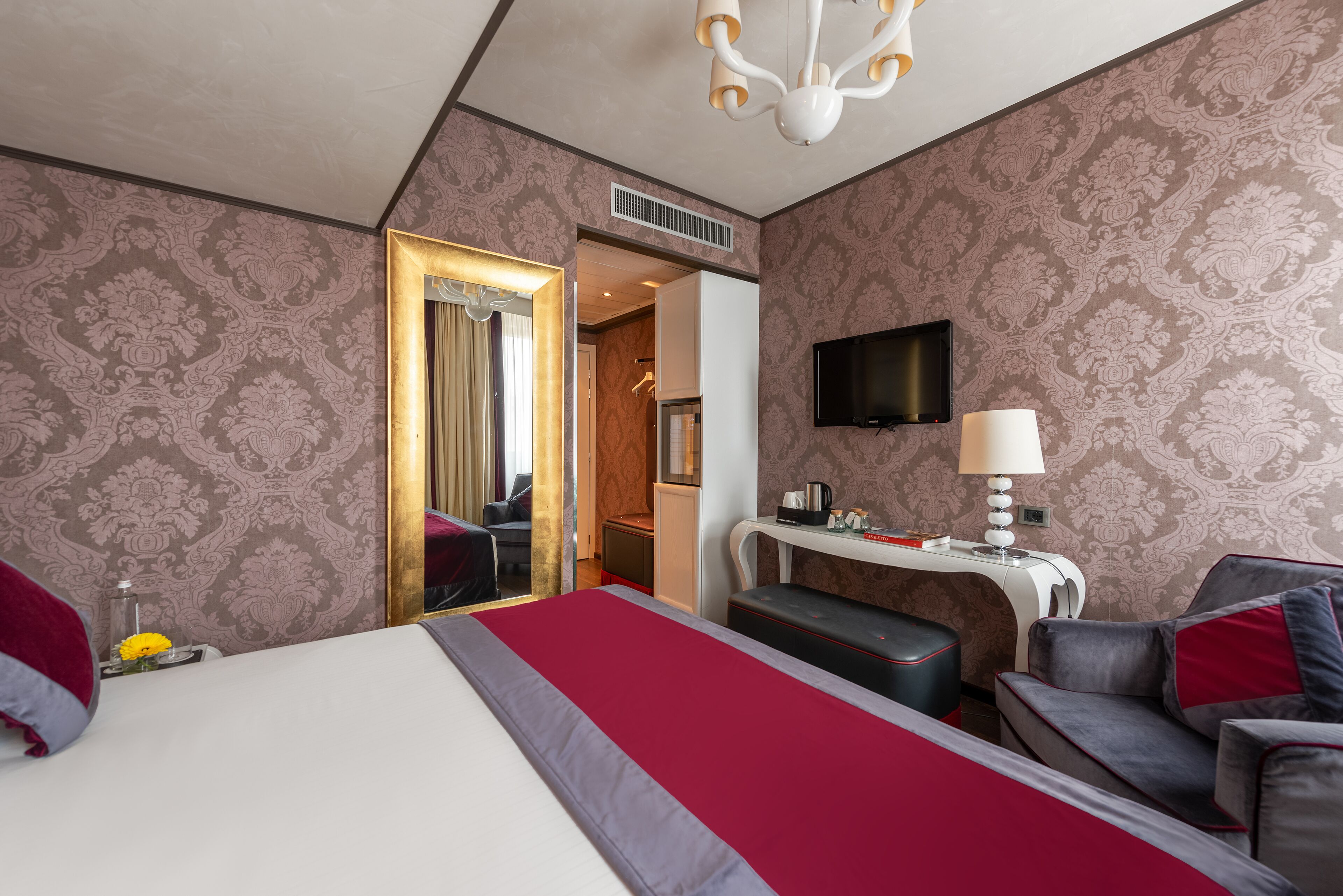 A hotel room with a bed, a desk, a chair, a television, and a mirror.