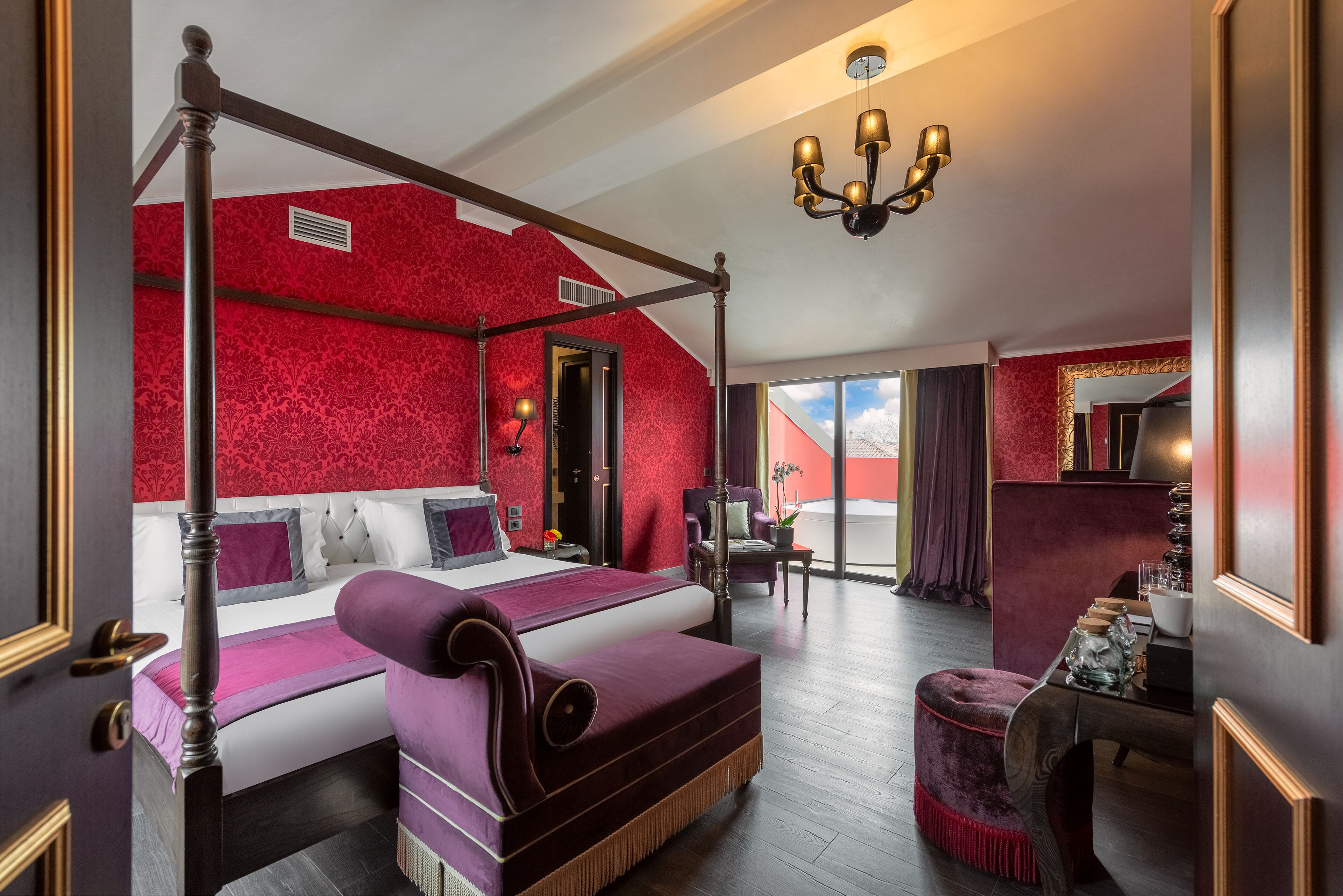A four-poster bed with a canopy, a chaise lounge, and a small table with a lamp.