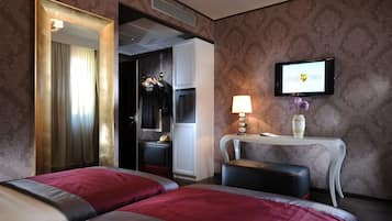 A hotel room with two beds, a vanity with a mirror, a television, and a small table with a lamp and decorative items.