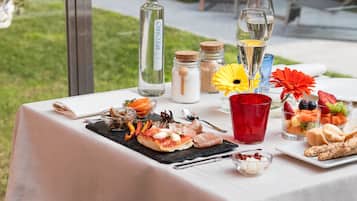 Mesa al aire libre con diversos alimentos y bebidas, incluyendo una botella de agua, vasos y una bandeja de frutas.