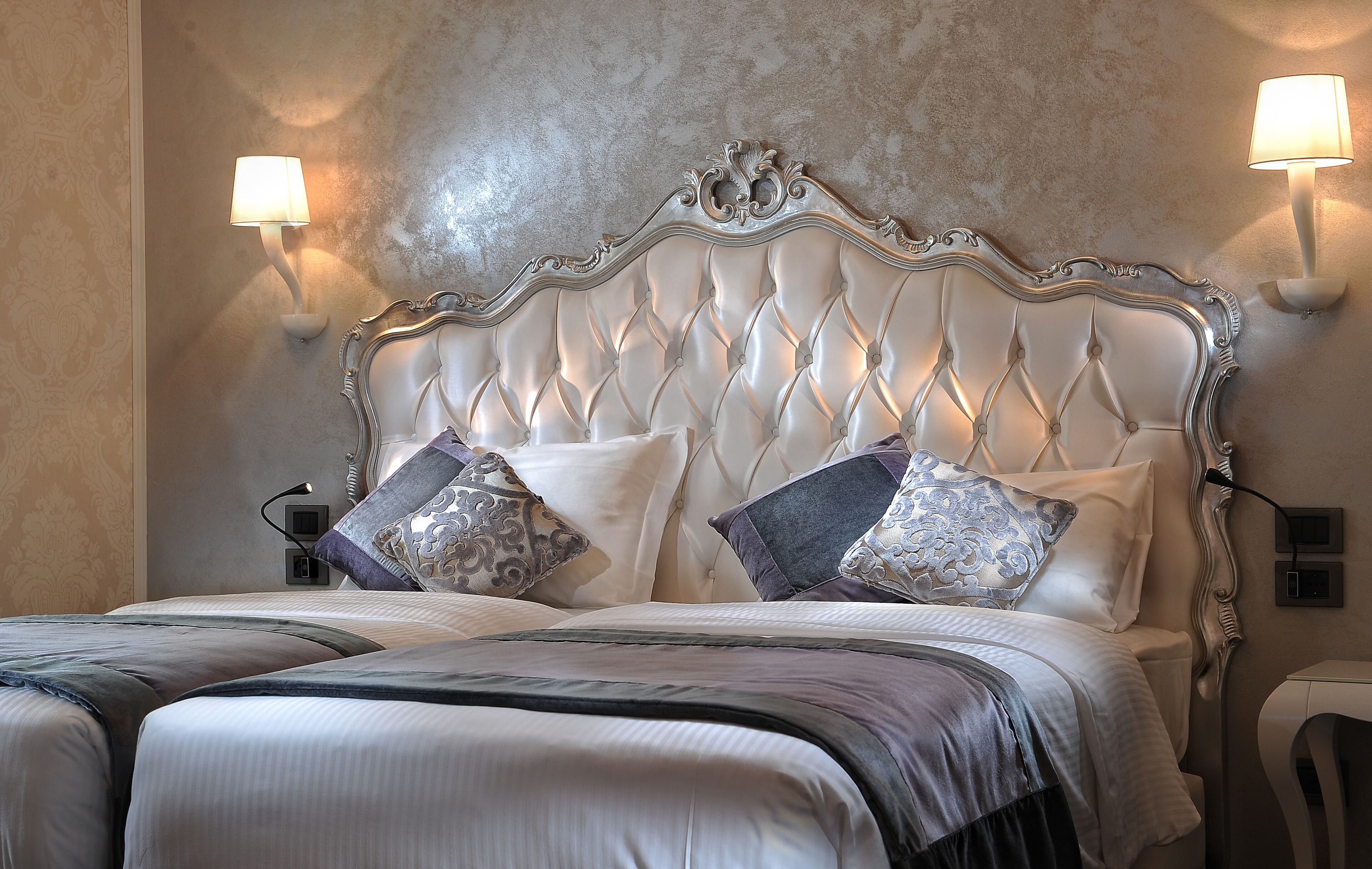 A bed with a tufted headboard, two wall-mounted lamps, and a bedside table with a lamp.