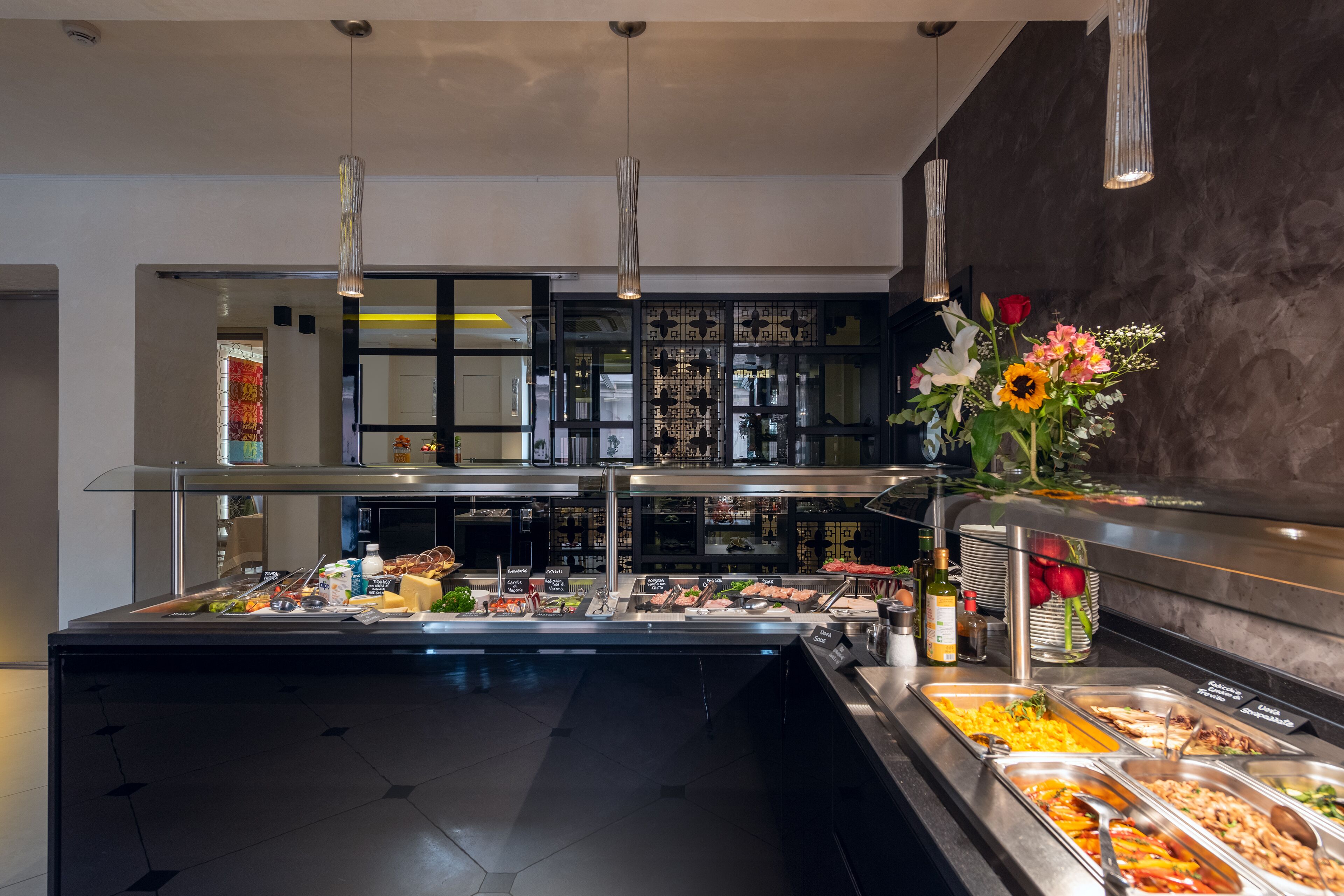 Een buffetgedeelte met diverse etenswaren, een glazen scheiding en een decoratieve vaas met bloemen.