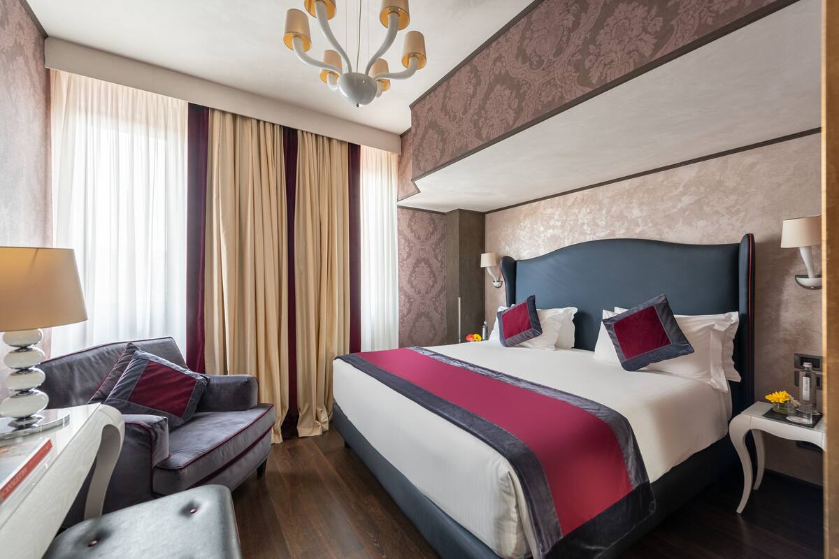 A hotel room with a large bed, a sofa, a desk, and a chandelier.