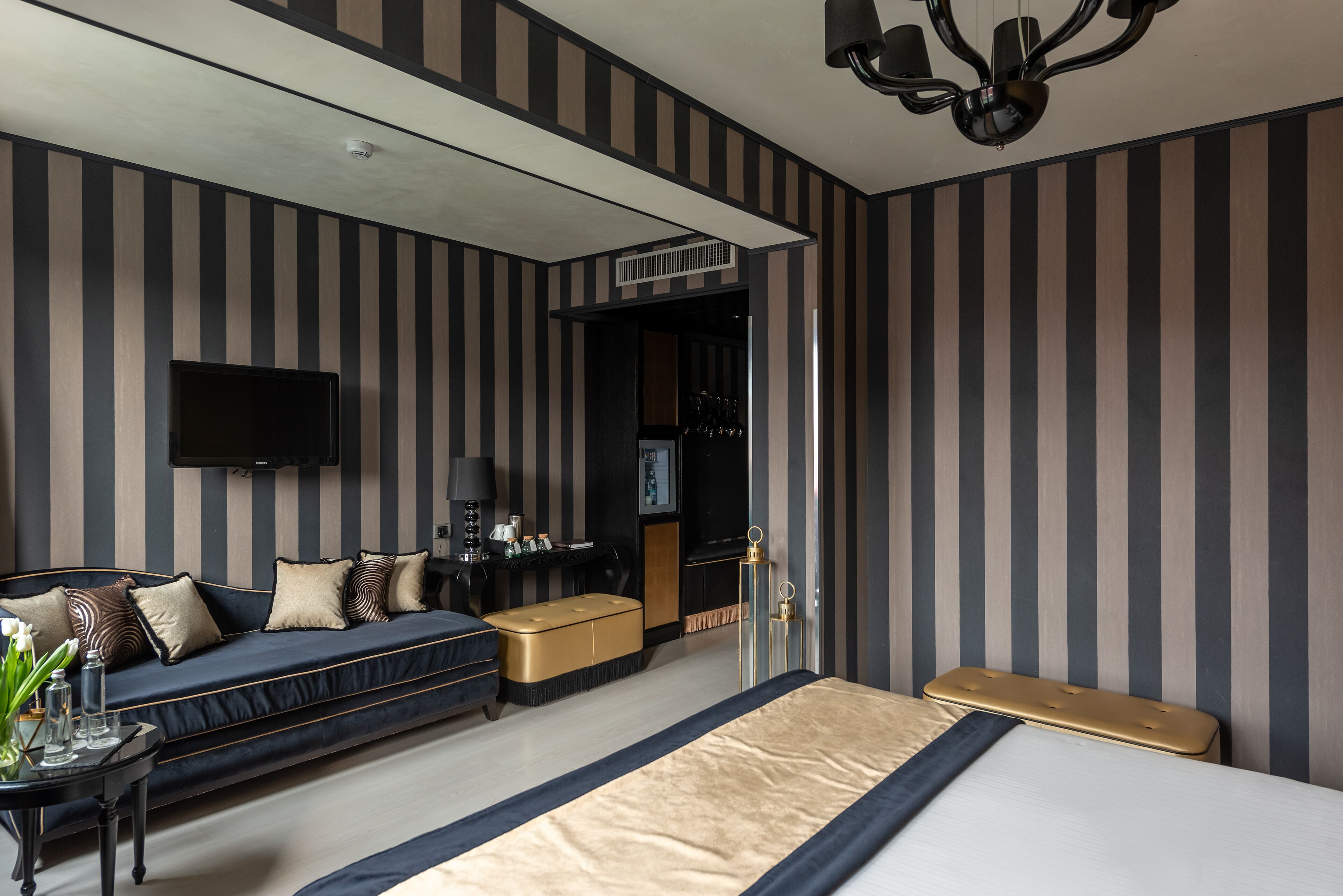 Una habitación de hotel moderna con diseño de pared a rayas, un sofá, una cama, un televisor y un escritorio con lámpara.