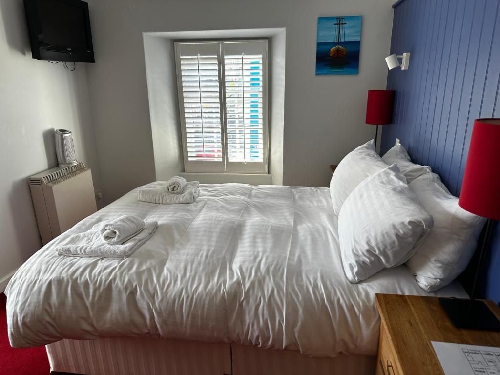 Quarto de hotel com cama, janela com persianas, quadro na parede e televisão fixada na parede.