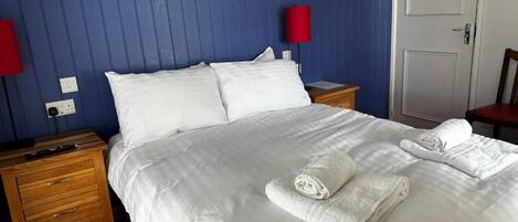 Een hotelkamer met een groot bed, twee nachtkastjes, een rode lamp en een deur.