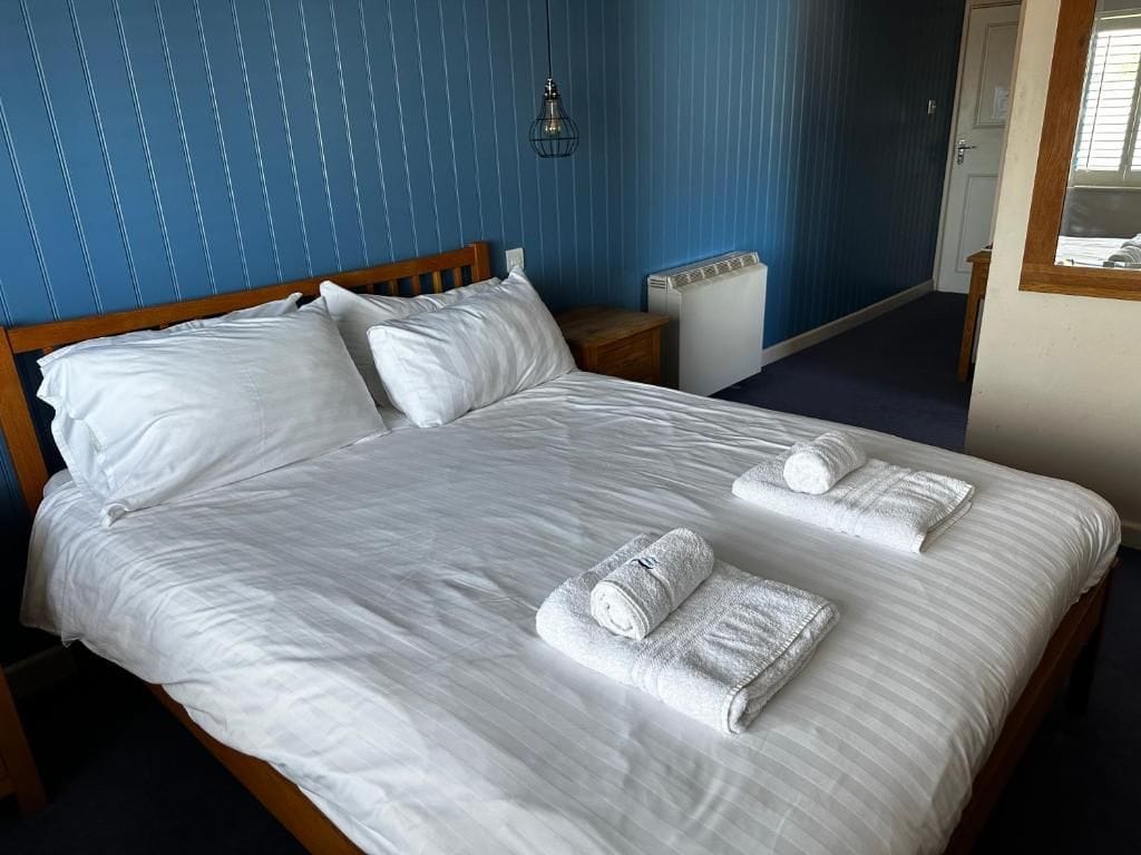 A neatly made bed with white linens and towels, a wooden headboard, a bedside table, and a radiator.